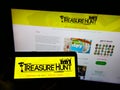 Person holding cellphone with logo of The Treasure Hunt Company (Brighton) on screen in front of business webpage.