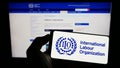 Person holding cellphone with logo of UN agency International Labour Organization (ILO) on screen in front of webpage.