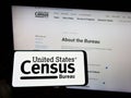 Person holding cellphone with logo of US agency United States Census Bureau (USCB) on screen in front of webpage.