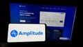 Person holding cellphone with logo of US analytics software company Amplitude Inc. on screen in front of business webpage.