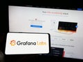 Person holding cellphone with logo of US analytics software company Grafana Labs on screen in front of business webpage.
