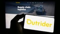 Person holding cellphone with logo of US company Outrider Technologies Inc. on screen in front of business webpage. Royalty Free Stock Photo