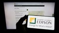 Person holding cellphone with logo of US company Southern California Edison (SCE) on screen in front of webpage.