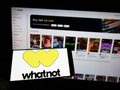 Person holding cellphone with logo of US e-commerce company Whatnot Inc. on screen in front of business webpage.