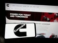 Person holding cellphone with logo of US manufacturing company Cummins Inc. on screen in front of business webpage.