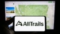 Person holding cellphone with logo of US outdoor platform company AllTrails LLC on screen in front of business webpage.
