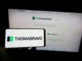 Person holding cellphone with logo of US private equity company Thoma Bravo L.P. on screen in front of business webpage.