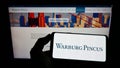 Person holding cellphone with logo of US private equity company Warburg Pincus LLC on screen in front of business web page.