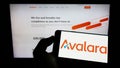 Person holding cellphone with logo of US software company Avalara Inc. on screen in front of business webpage.