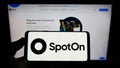 Person holding cellphone with logo of US software company SpotOn Transact LLC on screen in front of business webpage.