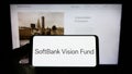 Person holding cellphone with logo of venture capital fund SoftBank Vision Fund on screen in front of business webpage.