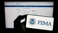 Person holding cellphone with seal of Federal Emergency Management Agency (FEMA) on screen in front of webpage.