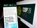 Person holding cellphone with web page of UN climate change conference COP28 (Dubai) on screen in front of logo.