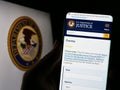 Person holding cellphone with web page of United States Department of Justice (DOJ) on screen in front of logo. Royalty Free Stock Photo