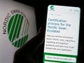 Person holding cellphone with webpage of environmental certification Nordic Ecolabel on screen in front of logo. Royalty Free Stock Photo