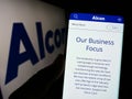 Person holding cellphone with webpage of eye care company Alcon AG on screen in front of business logo.