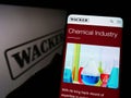 Person holding cellphone with webpage of German chemical company Wacker Chemie AG on screen in front of logo.