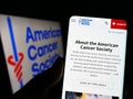 Person holding cellphone with webpage of organization American Cancer Society (ACS) on screen in front of logo.