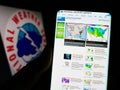 Person holding cellphone with webpage of US agency National Weather Service (NWS) on screen in front of logo.