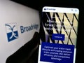 Person holding cellphone with webpage of US company Broadridge Financial Solutions Inc. on screen with logo.