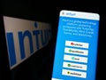 Person holding cellphone with webpage of US financial software company Intuit Inc. on screen in front of logo.