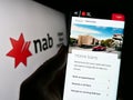 Person holding cellphone with website of company National Australia Bank Limited (NAB) on screen with logo.