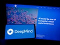 Person holding mobile phone with logo of AI company DeepMind Technologies Limited on screen in front of business web page.