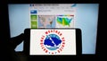 Person holding mobile phone with logo of American agency National Weather Service (NWS) on screen in front of web page.