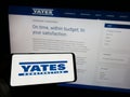 Person holding mobile phone with logo of American building company Yates Construction on screen in front of web page.