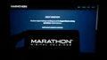 Person holding mobile phone with logo of American company Marathon Digital Holdings Inc. on screen in front of web page.