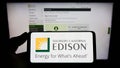 Person holding mobile phone with logo of American company Southern California Edison (SCE) on screen with web page.