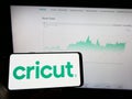 Person holding mobile phone with logo of American cutting plotter company Cricut Inc. on screen in front of web page.