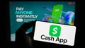 Person holding mobile phone with logo of American fintech company Cash App Investing LLC on screen in front of web page. Royalty Free Stock Photo