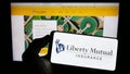 Person holding mobile phone with logo of American insurance company Liberty Mutual Group on screen in front of web page.