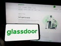 Person holding mobile phone with logo of American job review company Glassdoor Inc. on screen in front of web page. Royalty Free Stock Photo