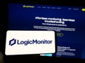 Person holding mobile phone with logo of American monitoring company LogicMonitor Inc. on screen in front of web page.