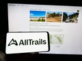 Person holding mobile phone with logo of American outdoor platform company AllTrails LLC on screen in front of web page.