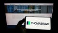 Person holding mobile phone with logo of American private equity company Thoma Bravo L.P. on screen in front of web page.