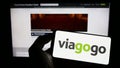 Person holding mobile phone with logo of American ticket exchange platform company Viagogo on screen in front of web page.