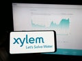 Person holding mobile phone with logo of American water technology company Xylem Inc. on screen in front of web page.