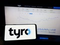 Person holding mobile phone with logo of Australian fintech company Tyro Payments Limited on screen in front of web page.