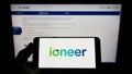 Person holding mobile phone with logo of Australian mining company company ioneer Ltd. on screen in front of web page.