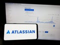 Person holding mobile phone with logo of Australian software company Atlassian Corporation on screen in front of web page.