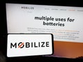 Person holding mobile phone with logo of automotive mobility company Mobilize on screen in front of business web page.