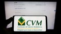 Person holding mobile phone with logo of Brazilian Comissao de Valores Mobiliarios (CVM) on screen in front of web page. Royalty Free Stock Photo