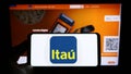 Person holding mobile phone with logo of Brazilian company Itau Unibanco Holding S.A. on screen in front of web page. Royalty Free Stock Photo