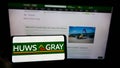 Person holding mobile phone with logo of British builders merchant company Huws Gray Limited on screen in front of webpage.