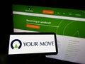 Person holding mobile phone with logo of British company Your-Move.co.uk Limited on screen in front of business web page.