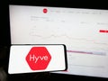 Person holding mobile phone with logo of British event management company Hyve Group plc on screen in front of web page.