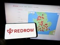 Person holding mobile phone with logo of British housebuilding company Redrow plc on screen in front of business web page.